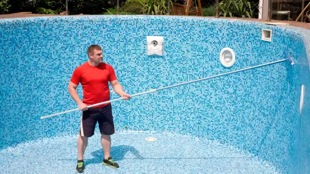 A guy in the center of a empty pool doing pool tile cleaning